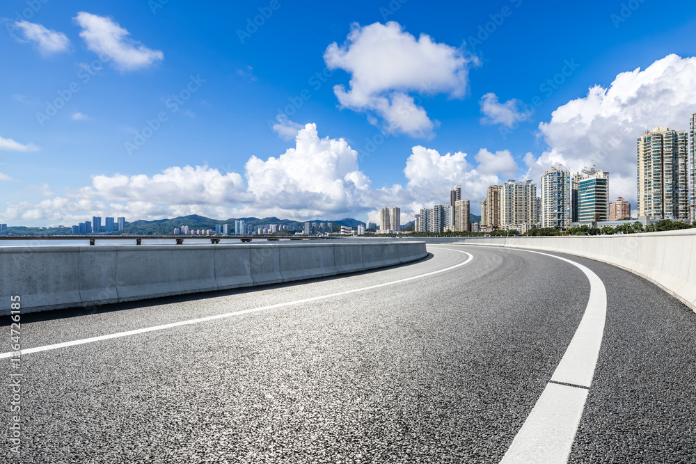 Asphalt road leading to the modern city under blue sky