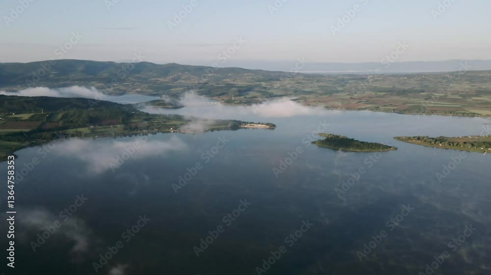 Beautiful aerial view of a tranquil lake surrounded by lush green hills during early morning hours Beautiful aerial view of a tranquil lake surrounded by lush green hills during early morning hours