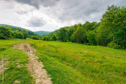 Obraz na płótnie dirt road through forested countryside. offroad path. beautiful summer rural landscape in mountains. adventure in nature scenery before the storm. dark sky w salonie