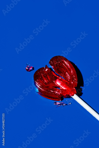 Broken heart-shaped lollipop on a blue background symbolizing heartbreak
