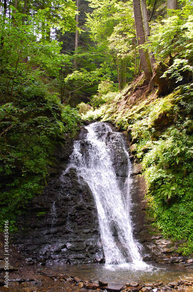 Obraz premium Scenic waterfall cascading down rocky cliffs in a lush green forest, creating a peaceful and refreshing natural landscape