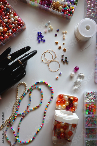 Hand figurine, colorful friendship bracelets, necklaces, various beads and DIY supplies on the table. Making jewelry at home. Flat lay.