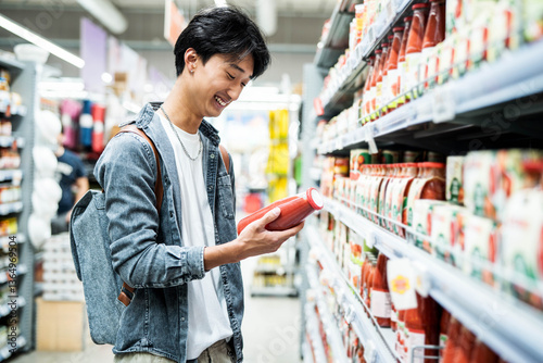 Foto Happy asian man holding bottle with tomato juice while shopping at grocery store