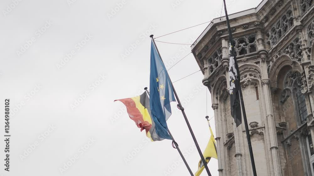 Bandiera Belga e bandiera Europea, riprese dal basso, durante una giornata nuvolosa. Città Europea