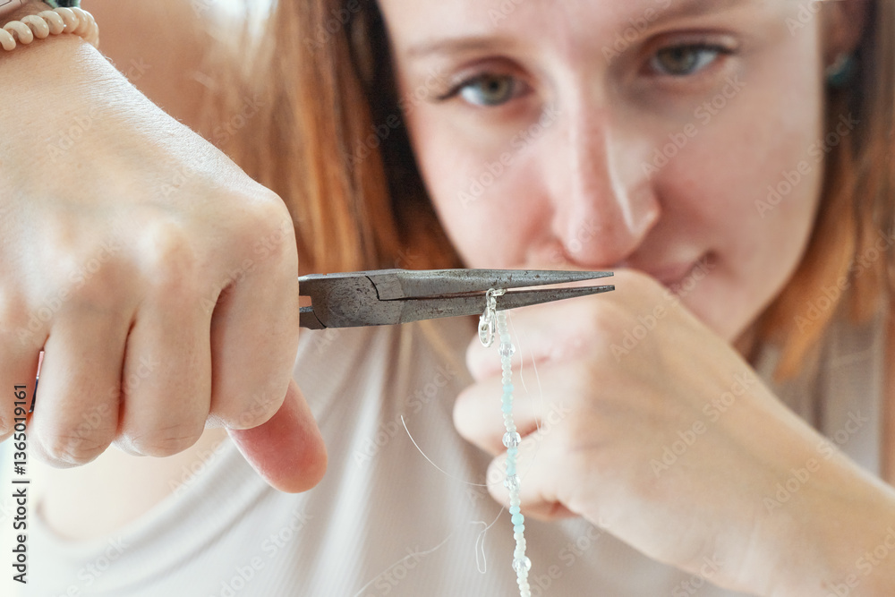 Obraz premium Closeup of woman face and hands with pliers making jewelry from beads at home. Focus on pliers. Art, hobby, handmade concept