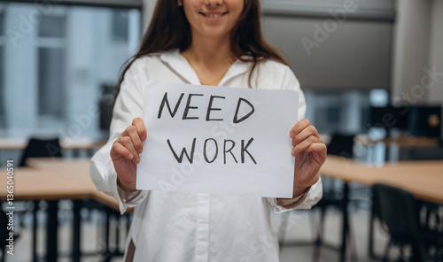 Close up view. Young woman in office holding banner with text of need work