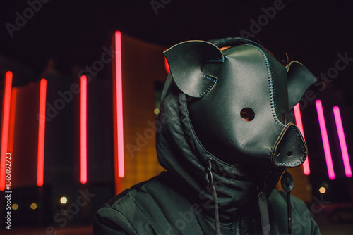 Slika na platnu A mysterious individual wearing a pig mask stands under vibrant neon lights, cap