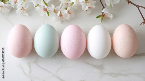 Colorful pastel eggs arranged neatly on a marble surface with delicate cherry blossom branches in the background during springtime