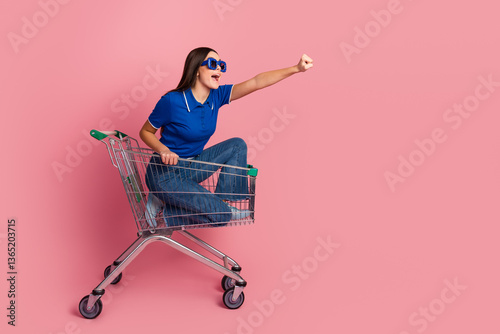 Young Woman Sitting in Shopping Cart Posing Enthusiastically On a Vibrant Pink Background photo