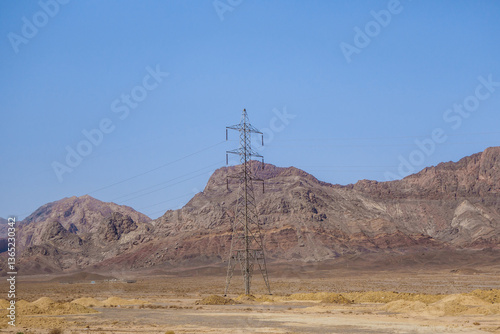 Power transmission line tower in a mountainous area. A service station is visible in the distance. Shot in Yazd Province, Iran