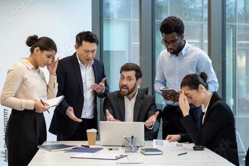 A diverse group of colleagues express frustration around a table with a laptop, showing disappointment with project outcomes and facing challenges photo