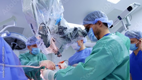 Bearded surgeon takes a tool device from assistant without distracting from microscope. Low angle view at the doctor performing neurosurgery.