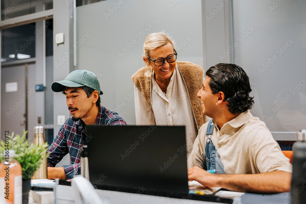 Smiling female professor talking with male student studying on laptop in university classroom Smiling female professor talking with male student studying on laptop in university classroom