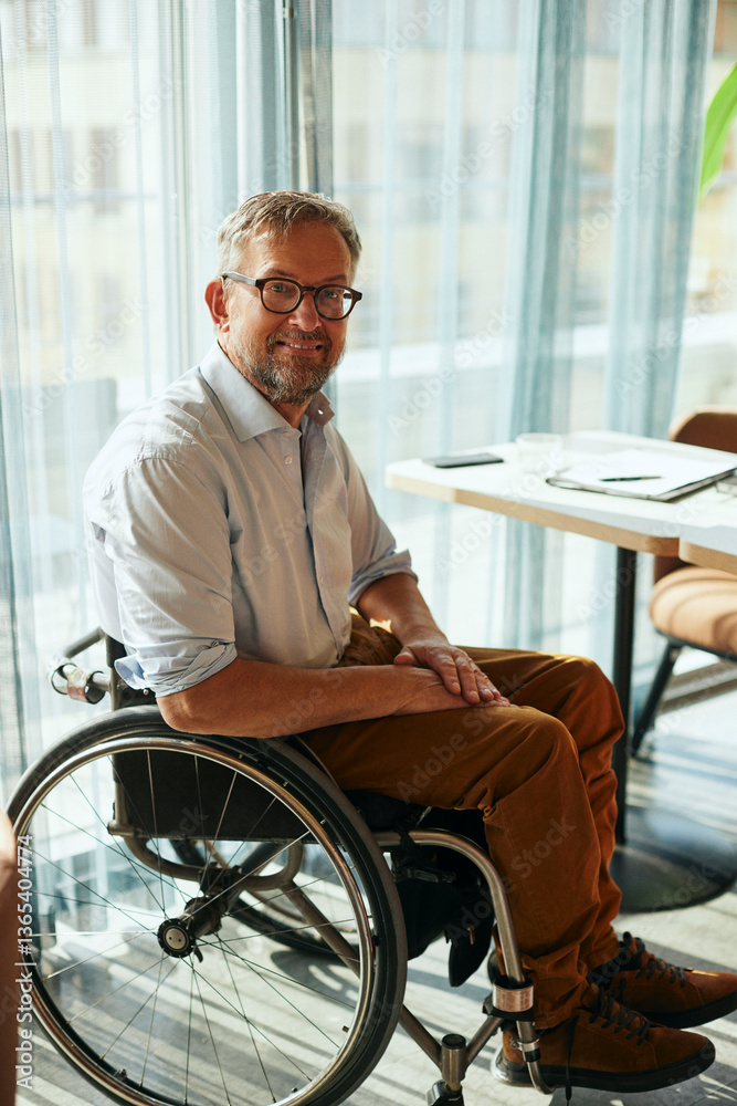 Portrait of smiling male entrepreneur with physical disability sitting on wheelchair in office Portrait of smiling male entrepreneur with physical disability sitting on wheelchair in office