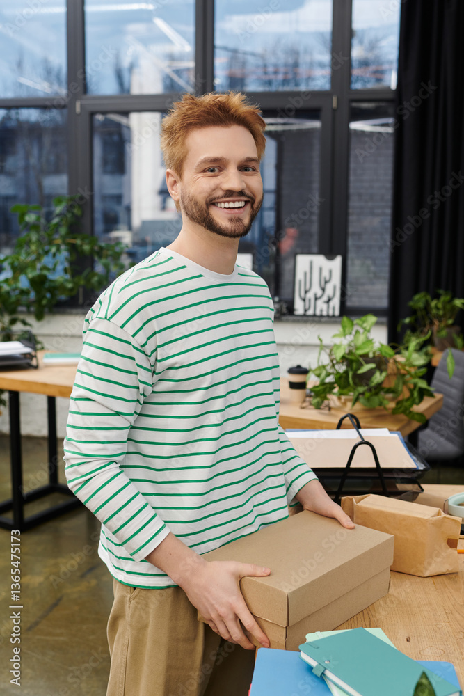 Fototapeta premium Smiling man enjoys the process of packing and moving in a modern workspace filled with plants