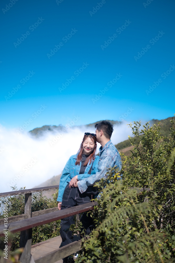 Naklejka premium A couple is standing on a wooden bridge, looking out over a mountain range