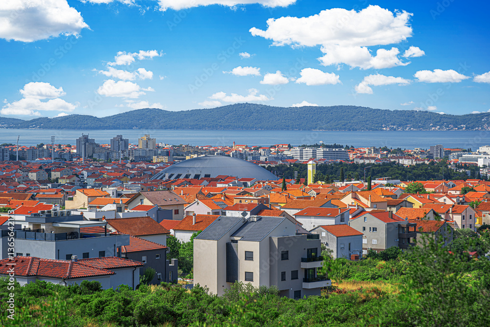 A stunning panoramic view of Zadar, Croatia, showcasing its iconic red rooftops, modern and historic architecture, and a breathtaking backdrop of the Adriatic Sea and distant mountains.