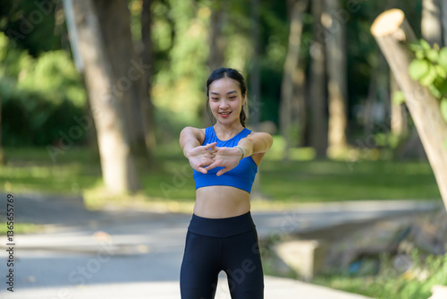 Young Asian sportswoman stretching arms in a park