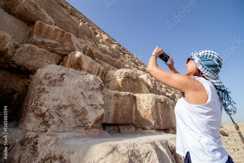A woman at the Giza plateau in Egypt, standing on the slopes and taking a picture of the Great Pyramid. Concept of vacation and travel to Africa.