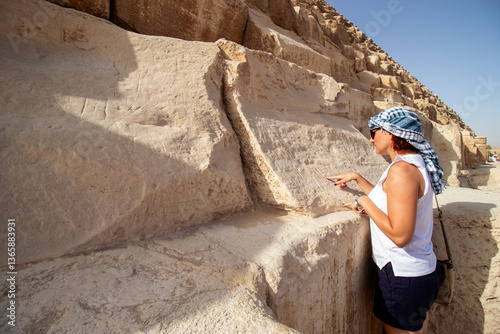 A woman at the Giza plateau in Egypt, standing on the slopes of the Great Pyramid and deciphers the inscription on a large stone block. Concept of adventure tourism.