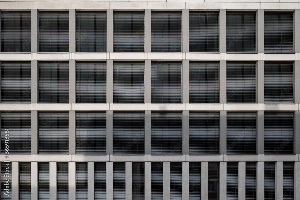 A contemporary architectural facade featuring a grid layout of rectangular windows with closed horizontal blinds. A contemporary architectural facade featuring a grid layout of rectangular windows with closed horizontal blinds.