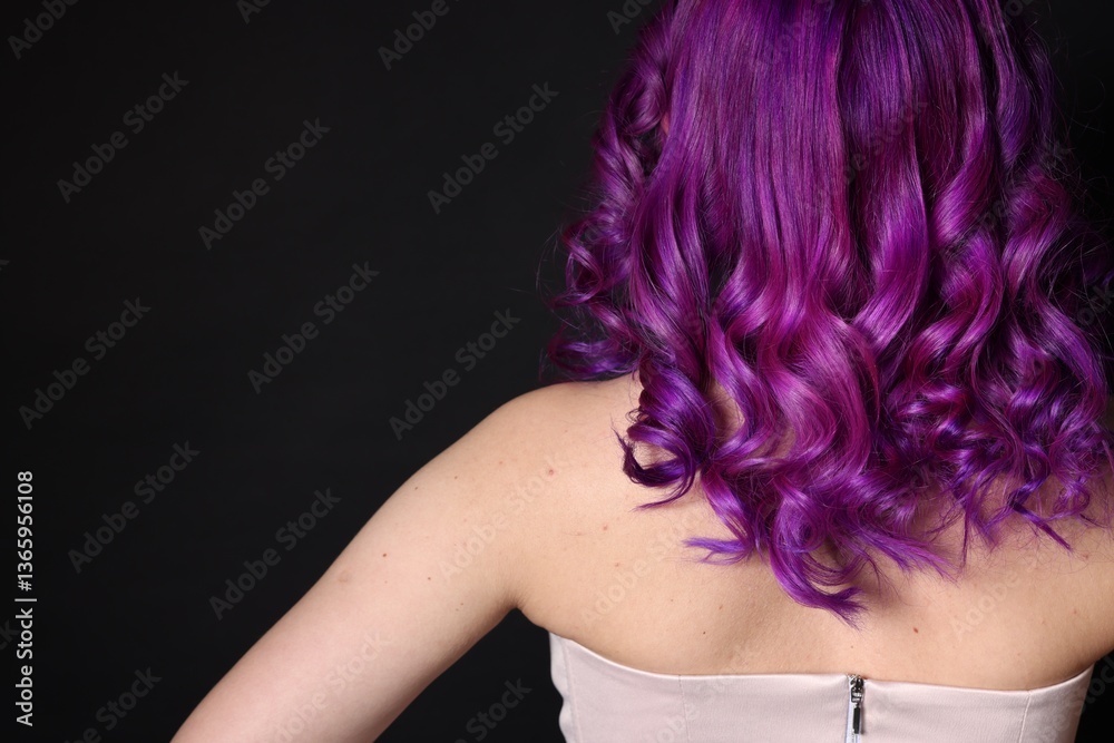 Fototapeta premium Beautiful woman with bright purple hair on black background, back view. Space for text