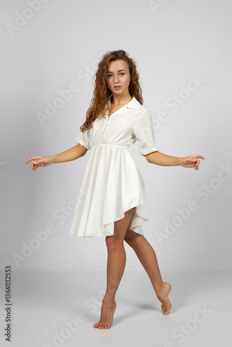 Young beautiful girl in a white dress posing for the camera in the studio on a gray background.