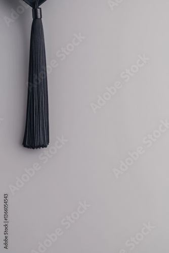 Elegant black tassel hanging against soft gray background, minim