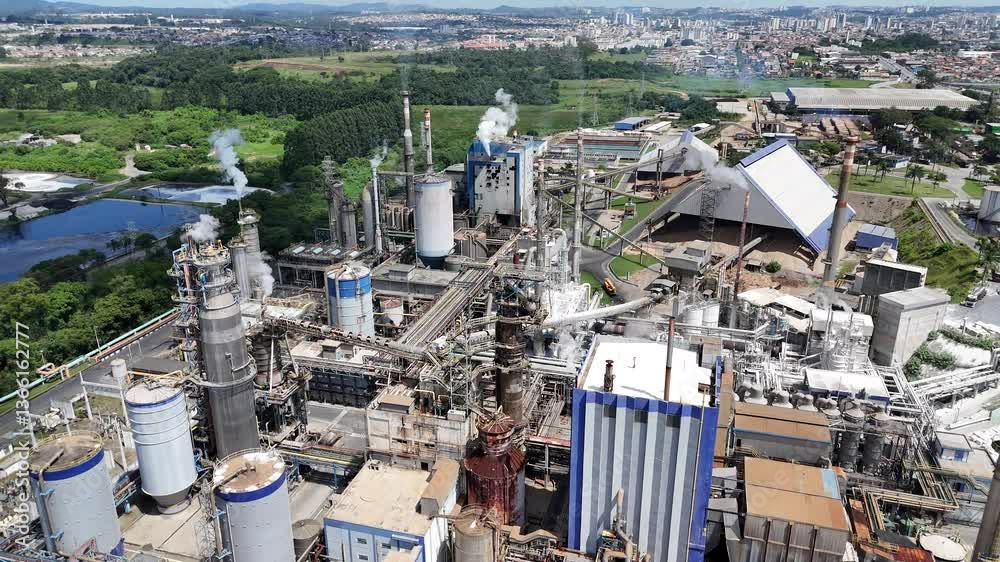 Visão aérea em vídeo 4k de uma planta industrial de papel e celulose com chaminés e caldeiras emitindo poluentes. A imagem destaca a produção industrial e o impacto ambiental. Capturada com drone