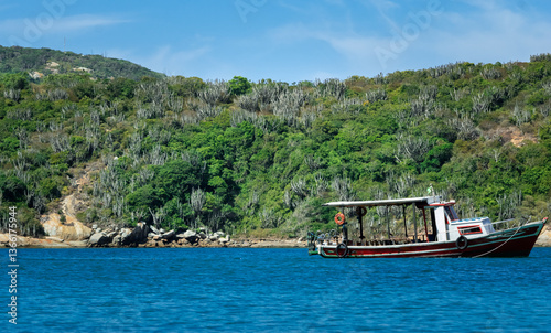 Beautiful sea with a boat, mountains around with lots of vegetation and blue sky, all this at Praia do Forno. Located near the city of Cabo Frio, Rio de Janeiro, Brazil.