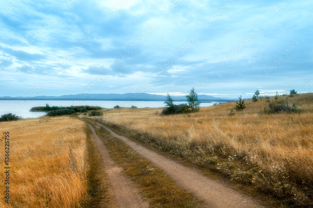 Fototapeta premium Summer cloudy landscape of the Irtyash lake, a lane leading to the lake and mountain range of the Ural mountains at the horizon in Southern Urals in Russia, soft filter applied