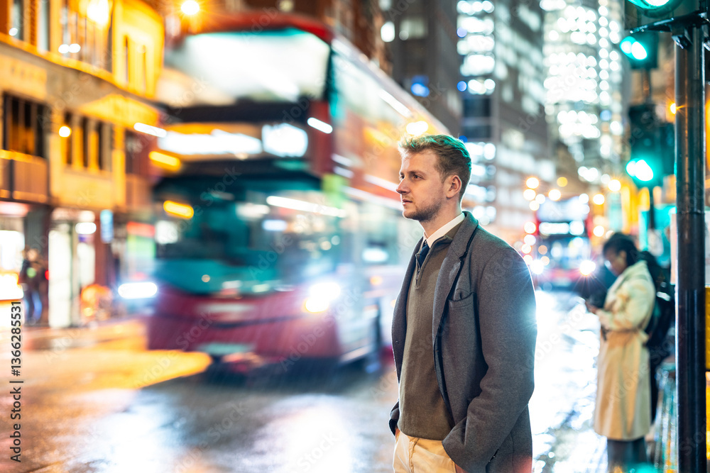 Businessman waiting for bus in London at night with green traffic light