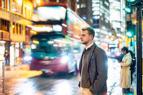 Obraz na płótnie Businessman waiting for bus in London at night with green traffic light w salonie