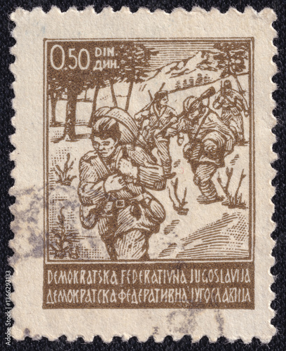 Yugoslav stamp issued in 1945 by the Democratic Federal Yugoslavia. Depicts armed partisans marching through a mountainous forest during WWII. Printed in brown monochrome. photo