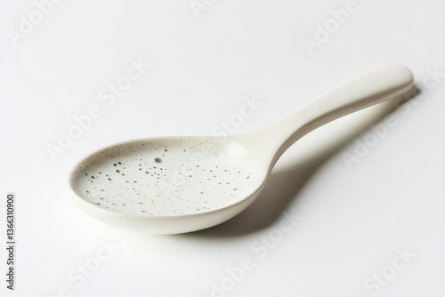 A white ceramic spoon with speckled detailing rests on a white background.