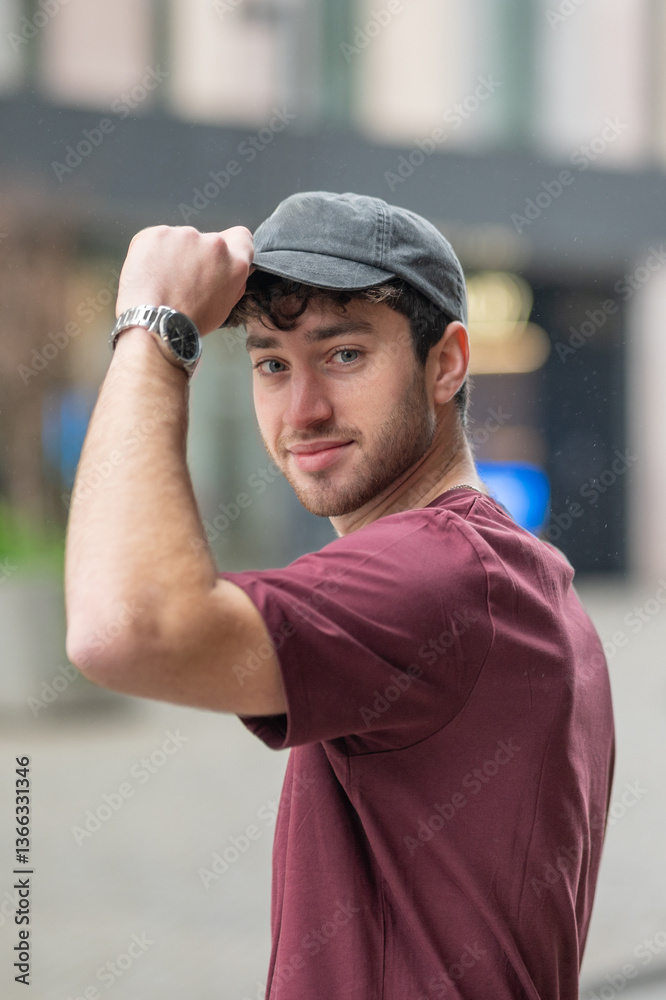Fototapeta premium Young man wearing a cap and adjusting it while smiling outdoors