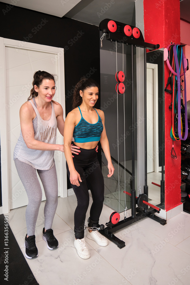 Woman using cable machine with personal trainer assisting her during workout session in gym
