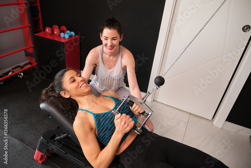 Obraz na płótnie Personal trainer assisting a smiling woman lifting weights with a cable machine in a gym w salonie