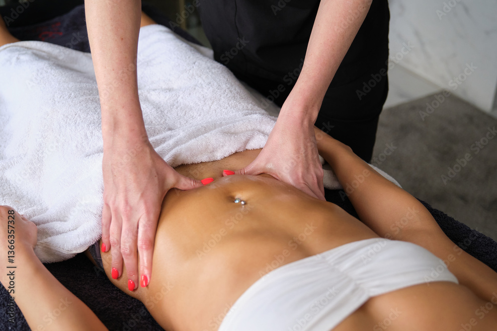 Masseuse applying pressure on stomach of young woman during slimming massage treatment