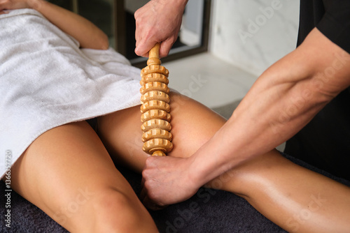 Obraz na płótnie Masseur using wooden roller tool massaging woman leg in spa salon w salonie