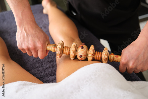 Masseur performing maderoterapia massage on woman's leg using wooden rolling pin tool