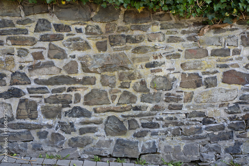 Stone wall made of antique old stone masonry  with ivy growing on it close up. Wallpaper concept