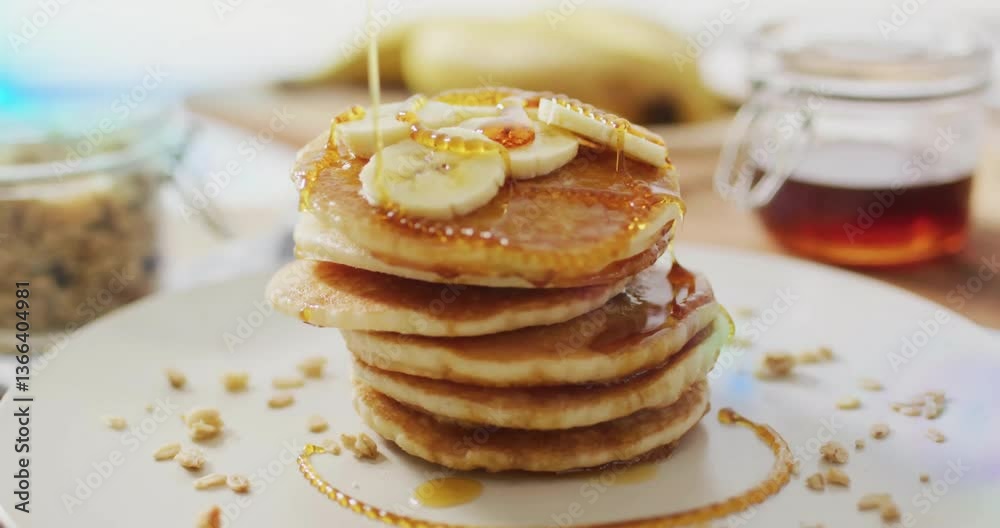Banana slices topping pancakes with syrup on white plate in kitchen Banana slices topping pancakes with syrup on white plate in kitchen