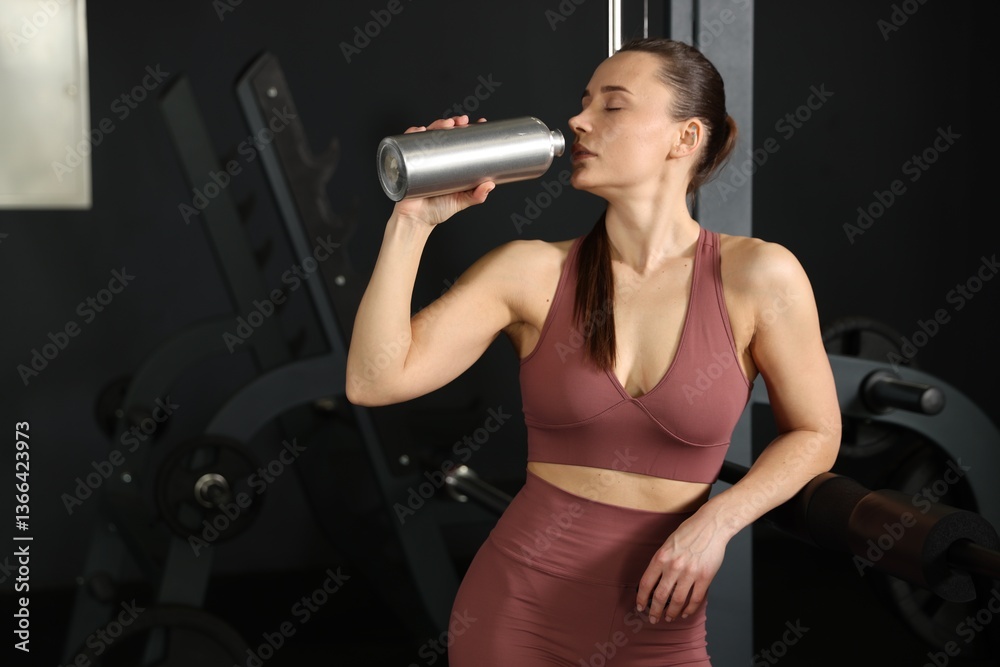 Fototapeta premium Athletic woman drinking from thermo bottle in gym. Space for text