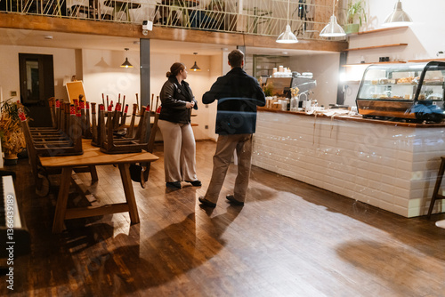 White female and male cafe owners are preparing and organizing their newly renovated cafe space for the opening, also with tables stacked and the counter setup for a fresh start.