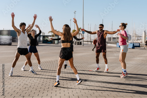A diverse group of five people exercises outdoors in a circle near a marina, wearing sportswear and performing jumping jacks under the sun. A concept of energy, fitness, and community. photo