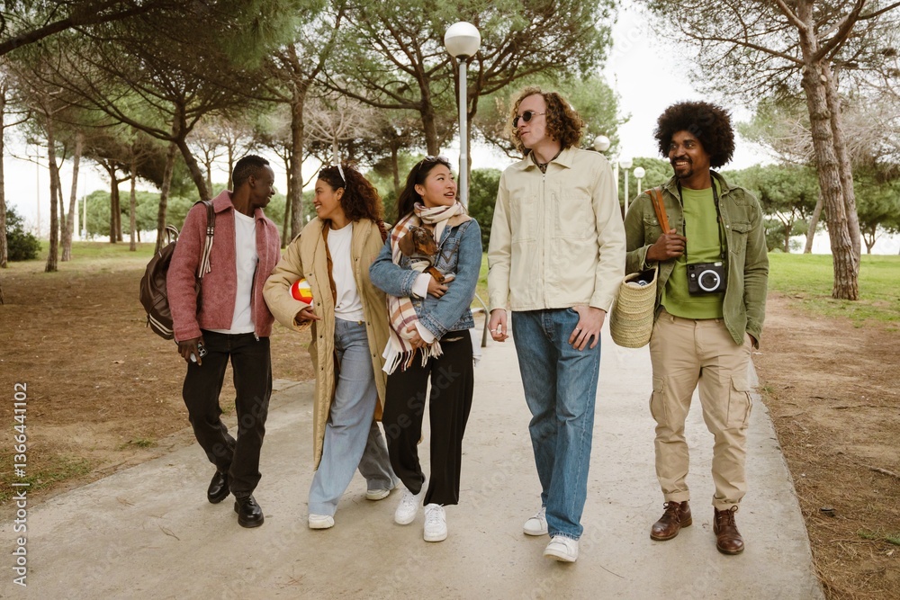 Obraz premium Five friends walk through a tree-lined park, chatting and laughing. One of them holds a dog, their loyal companion. A concept of friendship, adventure, and shared moments.