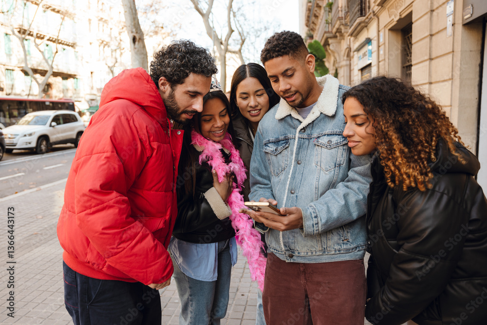 Obraz premium A group of five friends gathers on a city street, looking at a smartphone and smiling. They are dressed in warm jackets, with one person wearing a pink feather boa, suggesting a birthday celebration.
