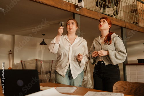 A female employee stands and looks in the direction indicated by the female owner standing next to her, preparing for the opening of the cafe