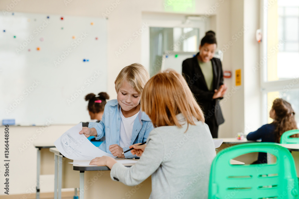 A schoolboy sits and holds a drawing while talking to a classmate sitting behind him, at school, in the classroom A schoolboy sits and holds a drawing while talking to a classmate sitting behind him, at school, in the classroom
